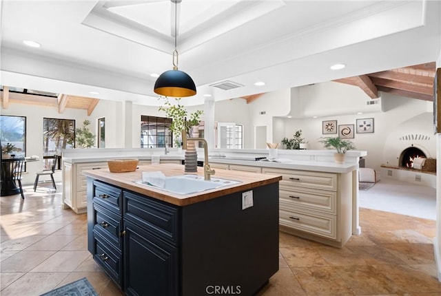 kitchen featuring lofted ceiling with beams, sink, hanging light fixtures, and a center island with sink