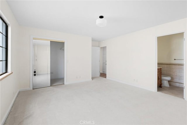 unfurnished bedroom featuring ensuite bath, a closet, and carpet