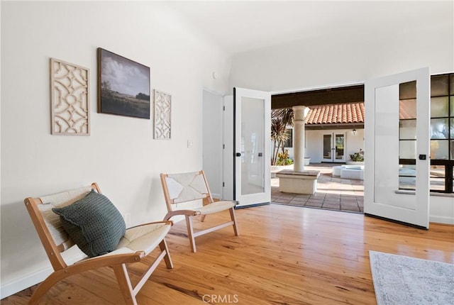 living area featuring french doors, wood-type flooring, and decorative columns