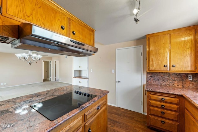 kitchen featuring tasteful backsplash, dark wood finished floors, brown cabinets, black electric cooktop, and under cabinet range hood