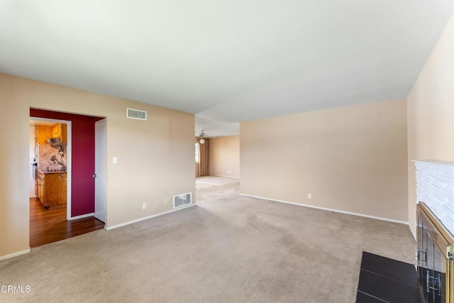 unfurnished living room featuring carpet floors, visible vents, and a fireplace with flush hearth