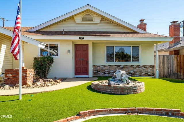 view of front of home featuring roof with shingles, a front yard, fence, and stucco siding