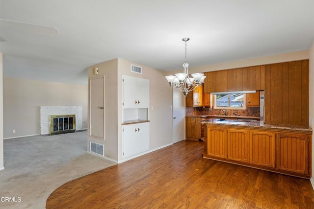 kitchen featuring pendant lighting, brown cabinets, visible vents, an inviting chandelier, and a brick fireplace