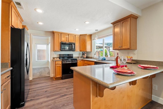 kitchen with sink, a breakfast bar area, decorative light fixtures, kitchen peninsula, and black appliances