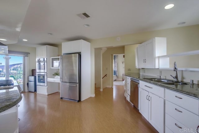 kitchen with sink, stainless steel appliances, dark stone counters, and white cabinets