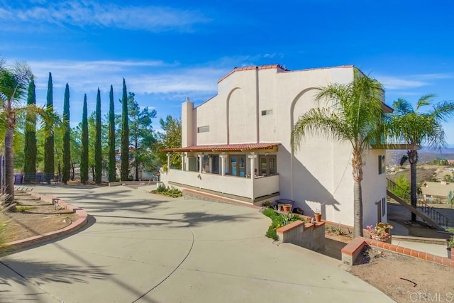 rear view of property featuring driveway, a tile roof, stairs, and stucco siding