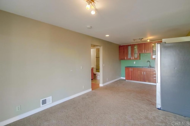 kitchen with a sink, visible vents, freestanding refrigerator, brown cabinetry, and glass insert cabinets