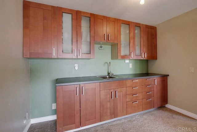 kitchen with glass insert cabinets, brown cabinetry, a sink, and baseboards