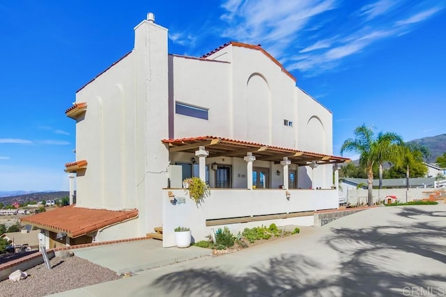 exterior space featuring a tiled roof, a chimney, and stucco siding