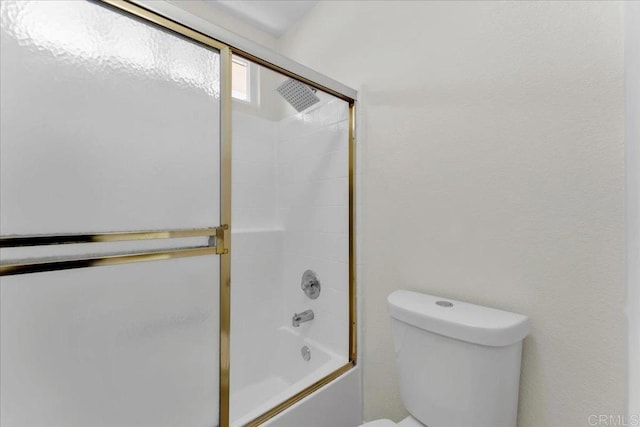 bathroom featuring toilet and bath / shower combo with glass door