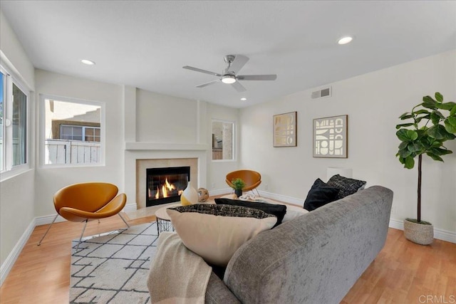 living room featuring a premium fireplace, ceiling fan, and light hardwood / wood-style floors