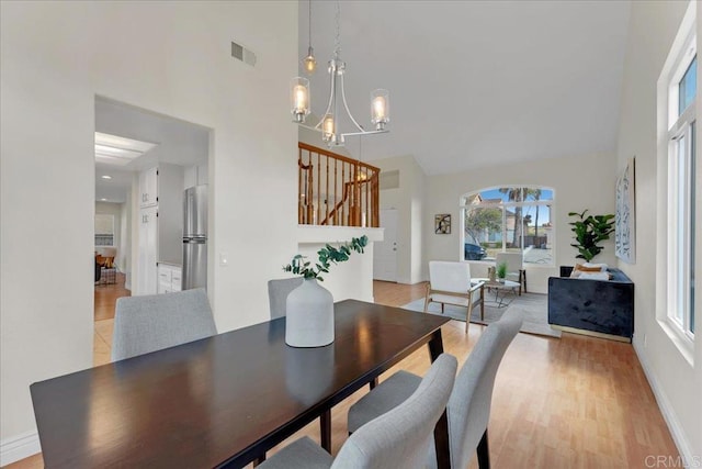 dining area featuring light hardwood / wood-style floors, high vaulted ceiling, and a notable chandelier