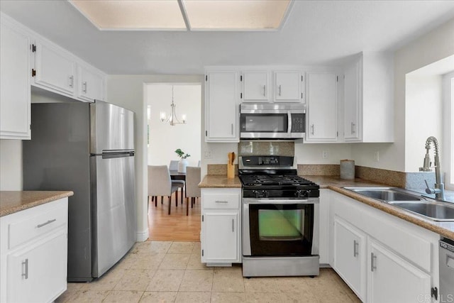 kitchen featuring appliances with stainless steel finishes, pendant lighting, sink, white cabinets, and a notable chandelier