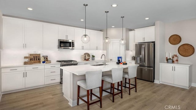 kitchen featuring appliances with stainless steel finishes, pendant lighting, white cabinetry, an island with sink, and sink