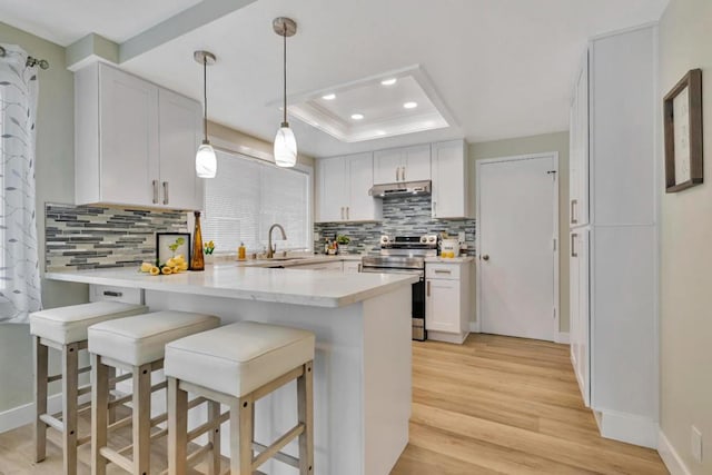 kitchen featuring a kitchen bar, white cabinetry, stainless steel electric range oven, a tray ceiling, and kitchen peninsula