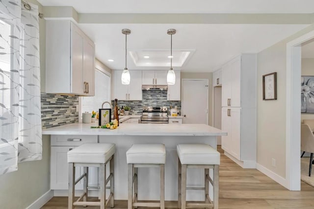 kitchen with stainless steel range with electric stovetop, hanging light fixtures, white cabinetry, a kitchen breakfast bar, and a tray ceiling