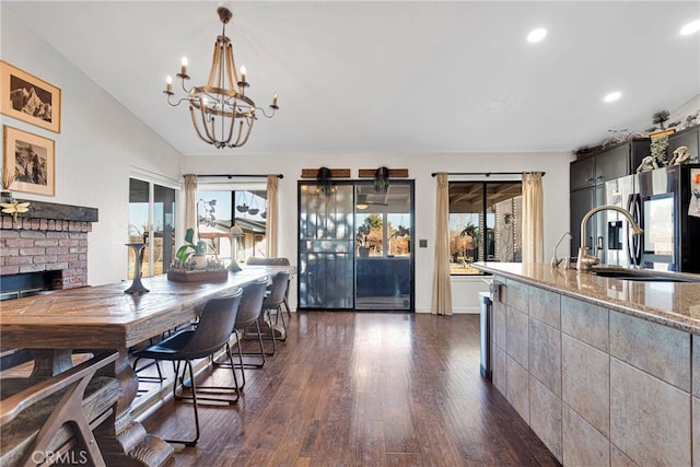 dining area with sink, an inviting chandelier, dark hardwood / wood-style floors, a brick fireplace, and vaulted ceiling