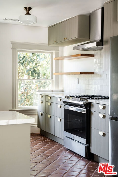 kitchen featuring backsplash, stainless steel appliances, gray cabinets, and wall chimney range hood