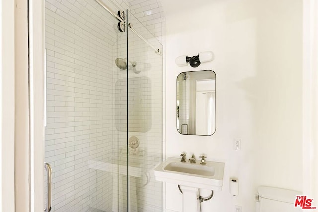 bathroom featuring a shower with door, sink, and toilet