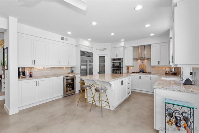 kitchen with a kitchen island, sink, white cabinets, beverage cooler, and wall chimney range hood