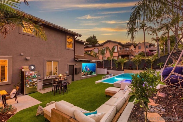 pool at dusk featuring a patio, an outdoor hangout area, and a lawn