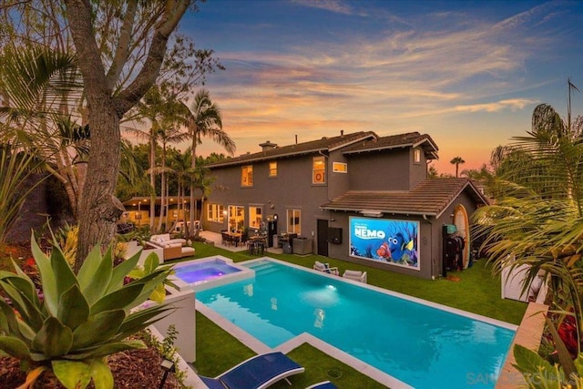 pool at dusk featuring an in ground hot tub, an outdoor hangout area, a patio, and a lawn