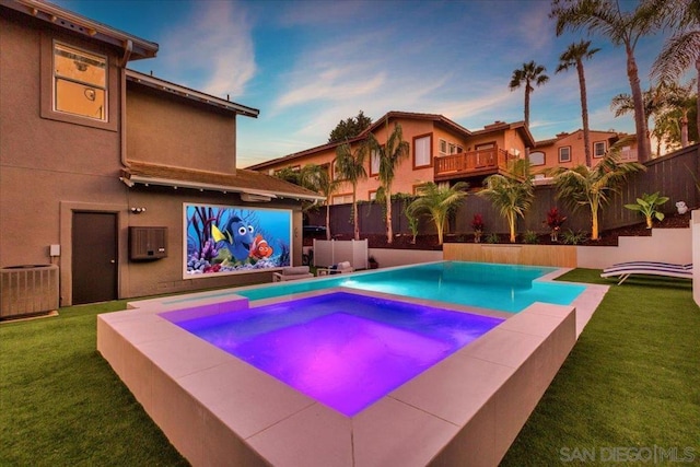 pool at dusk with an in ground hot tub, central AC unit, and a lawn