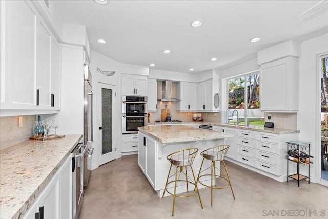 kitchen with wall chimney range hood, a breakfast bar, stainless steel appliances, a center island, and white cabinets