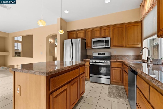 kitchen with sink, light tile patterned floors, appliances with stainless steel finishes, dark stone countertops, and a center island