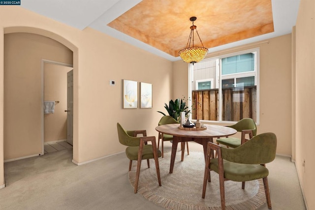 dining area with a tray ceiling and light colored carpet