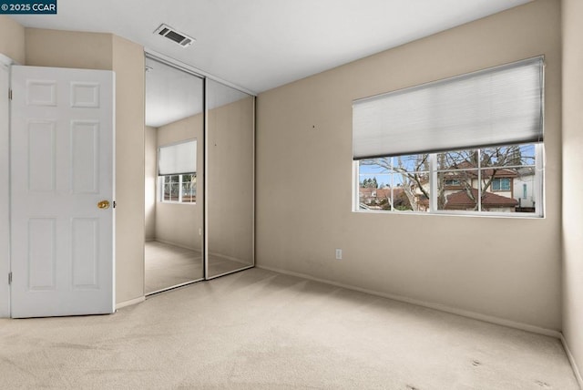 unfurnished bedroom featuring multiple windows, a closet, and light carpet