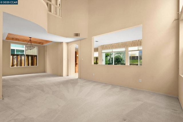 unfurnished room with a towering ceiling, light colored carpet, and a notable chandelier