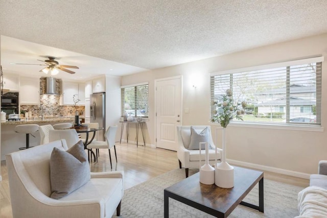 living room featuring ceiling fan, light hardwood / wood-style flooring, and a textured ceiling