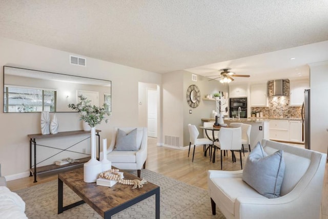 living room with sink, a textured ceiling, ceiling fan, and light wood-type flooring