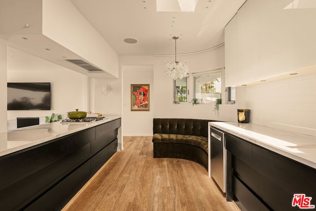 interior space featuring a skylight, decorative light fixtures, white cabinetry, light hardwood / wood-style floors, and white gas cooktop