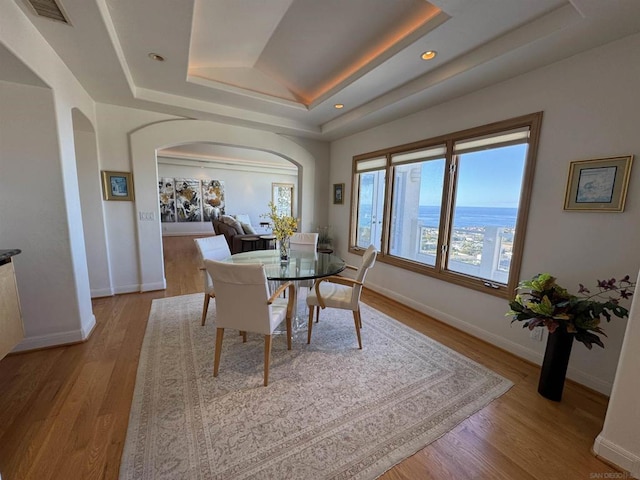 dining space featuring a water view, light hardwood / wood-style flooring, and a tray ceiling