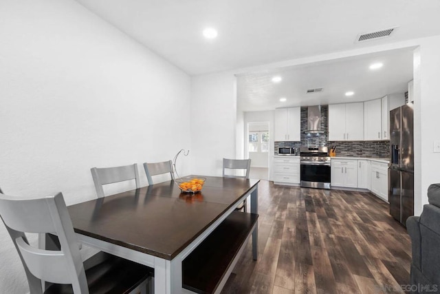 kitchen with dark wood-type flooring, white cabinetry, stainless steel appliances, decorative backsplash, and wall chimney range hood