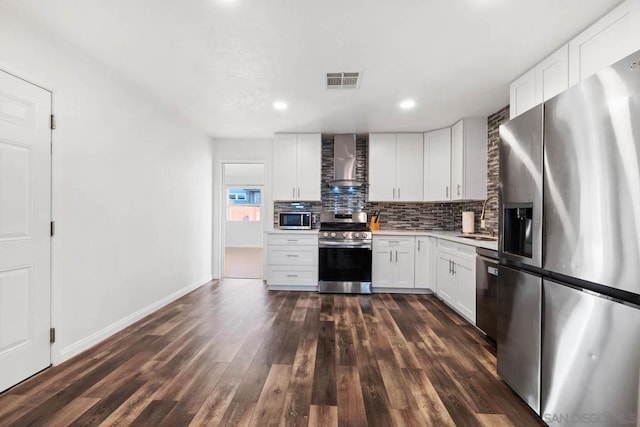 kitchen featuring wall chimney range hood, dark wood-type flooring, stainless steel appliances, tasteful backsplash, and white cabinets