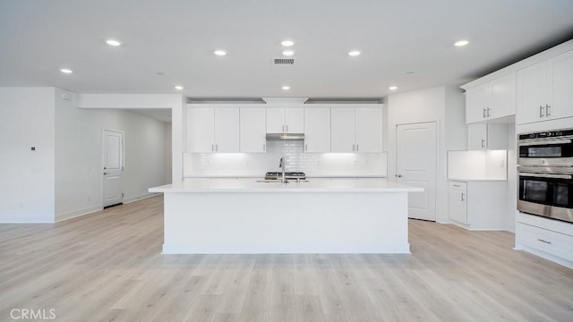 kitchen featuring visible vents, light wood-type flooring, light countertops, and a kitchen island with sink