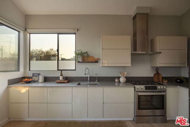 kitchen featuring white cabinets, stainless steel gas range, sink, and wall chimney range hood