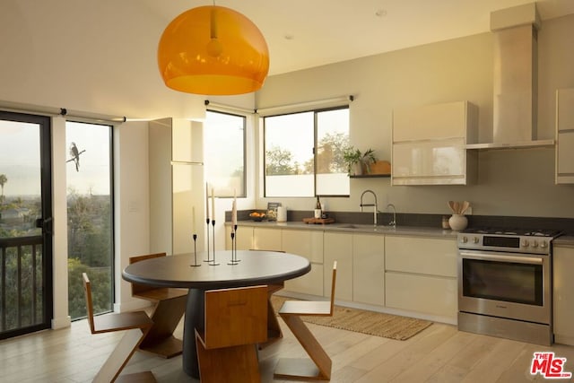 kitchen featuring gas range, sink, white cabinets, and wall chimney exhaust hood