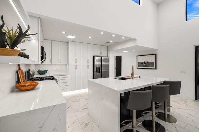 kitchen with sink, white cabinetry, light stone counters, a center island with sink, and appliances with stainless steel finishes