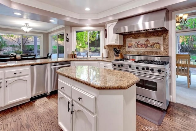 kitchen with white cabinetry, appliances with stainless steel finishes, wall chimney exhaust hood, and a center island