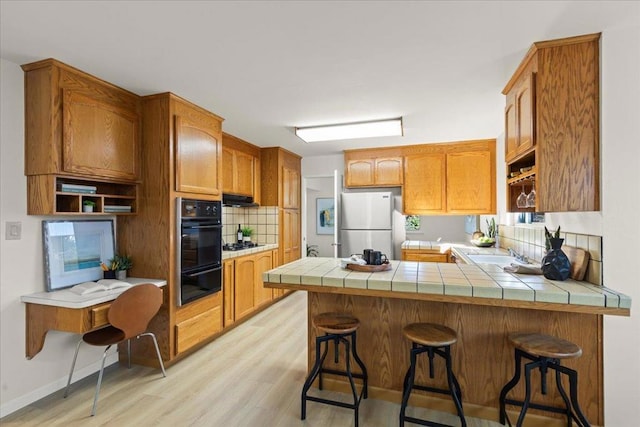 kitchen with tile counters, kitchen peninsula, a kitchen bar, and black appliances