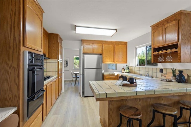 kitchen with tasteful backsplash, tile countertops, light wood-type flooring, stainless steel refrigerator, and kitchen peninsula