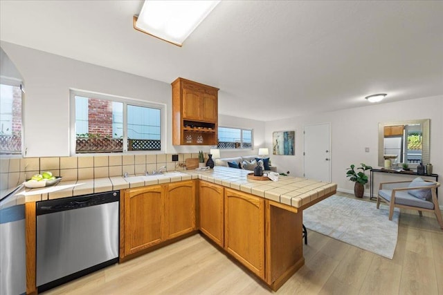 kitchen with tile countertops, stainless steel dishwasher, kitchen peninsula, light hardwood / wood-style floors, and backsplash