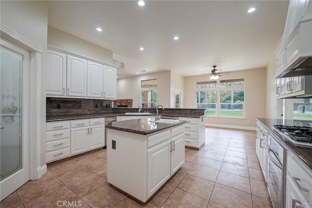 kitchen with appliances with stainless steel finishes, tasteful backsplash, white cabinetry, sink, and a center island with sink