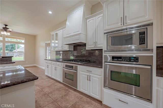 kitchen with dark stone countertops, white cabinets, backsplash, custom exhaust hood, and stainless steel appliances