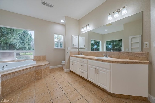 bathroom featuring tile patterned flooring, vanity, a relaxing tiled tub, and toilet