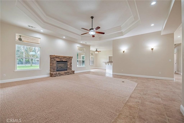 unfurnished living room featuring crown molding, a tray ceiling, a stone fireplace, and a healthy amount of sunlight